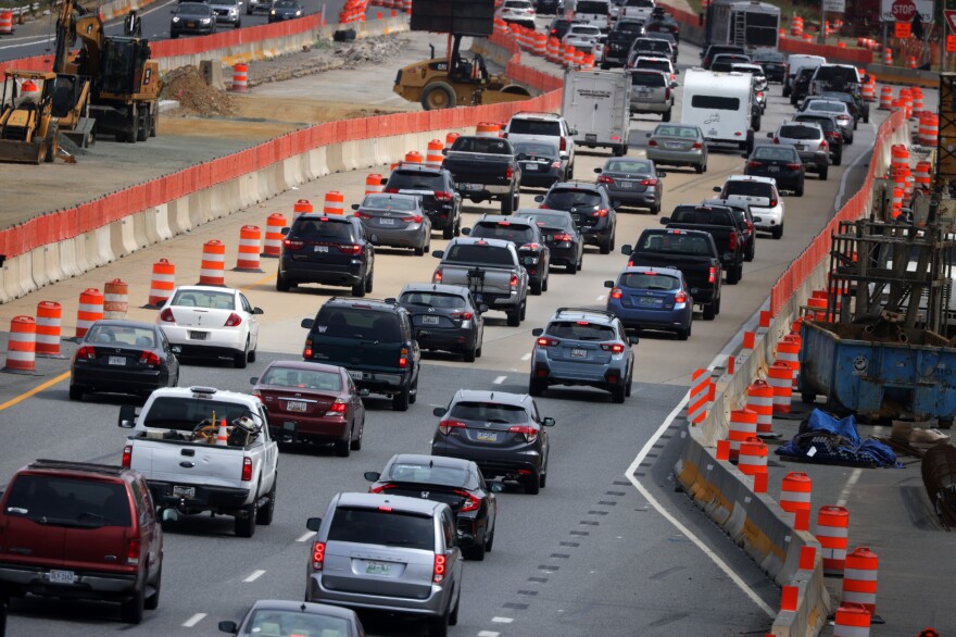 Cars line up on a three-lane highway of standstill traffic, framed by orange cones.
