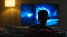 A photo of the back view of a man sitting on a couch watching tv. 