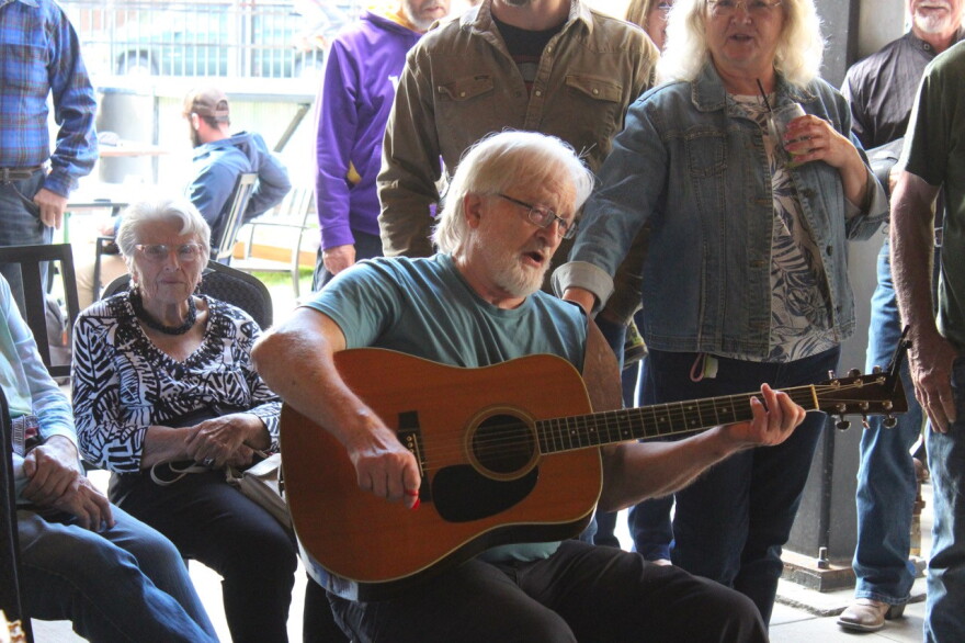 A man in the center plays his guitar with others surrounding him.