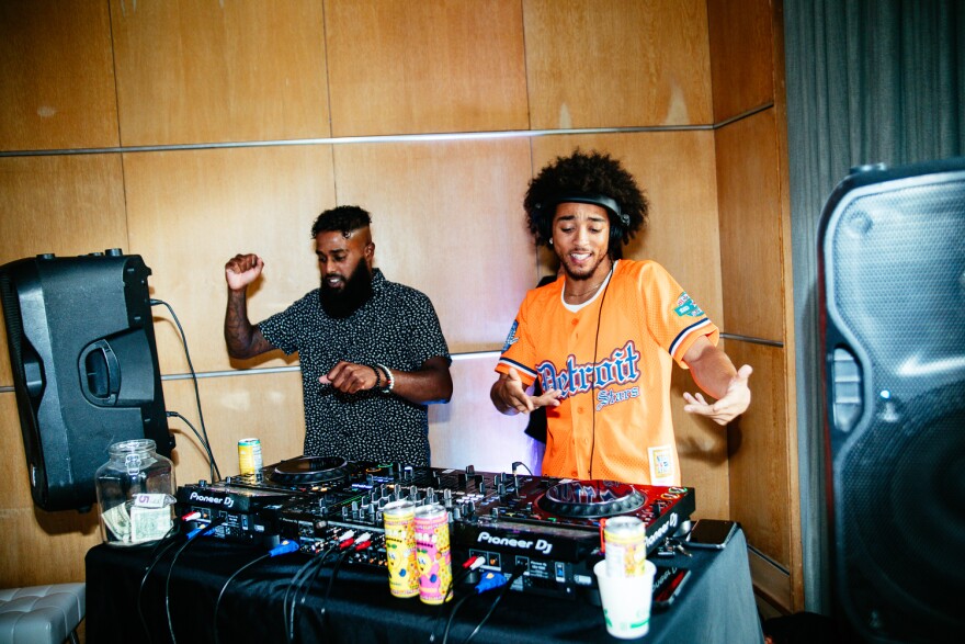 Two DJs dance behind their booth.