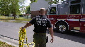 A member of the Florence, Ky., Police Department moves yellow police tape to allow an engine to pass into the area where a shooting took place, Saturday, July 6, 2024, in Florence, Ky. Police say several people were killed and others wounded in an early morning shooting during a party at this home in northern Kentucky. Police say the shooting suspect later died after fleeing the home and leading police on a vehicle pursuit that ended with the suspect's car falling into a ditch. (AP Photo/Carolyn Kaster)