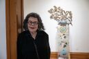 A woman wearing glasses and a black outfit standing in a doorway with a teapot sculpture in the background.