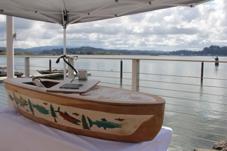A canoe with salmon and tree designs next to water.