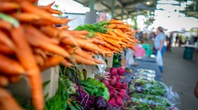 Passersby look at carrots, radishes and beets at a farmers market in Edmond.