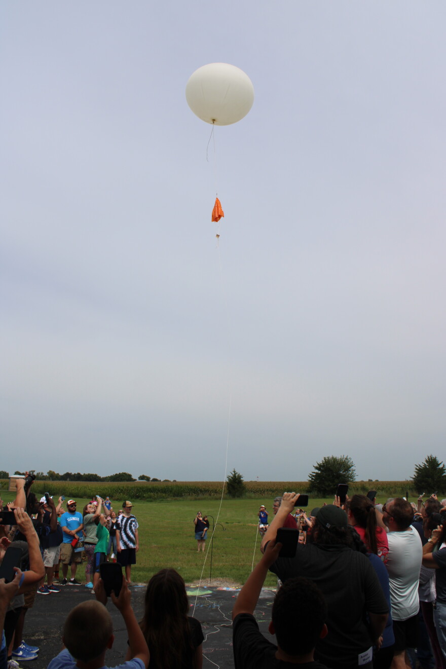 A crowd gazes up and photographs a weather balloon that was launched. 