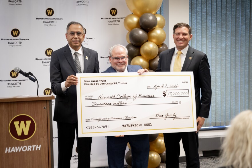 Three men stand next to a podium bearing the WMU logo and "Haworth", with a white WMU backdrop behind them. They hold a large check for $17 million dollars.