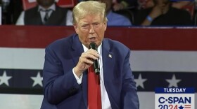 man in suit and red tie holds mic