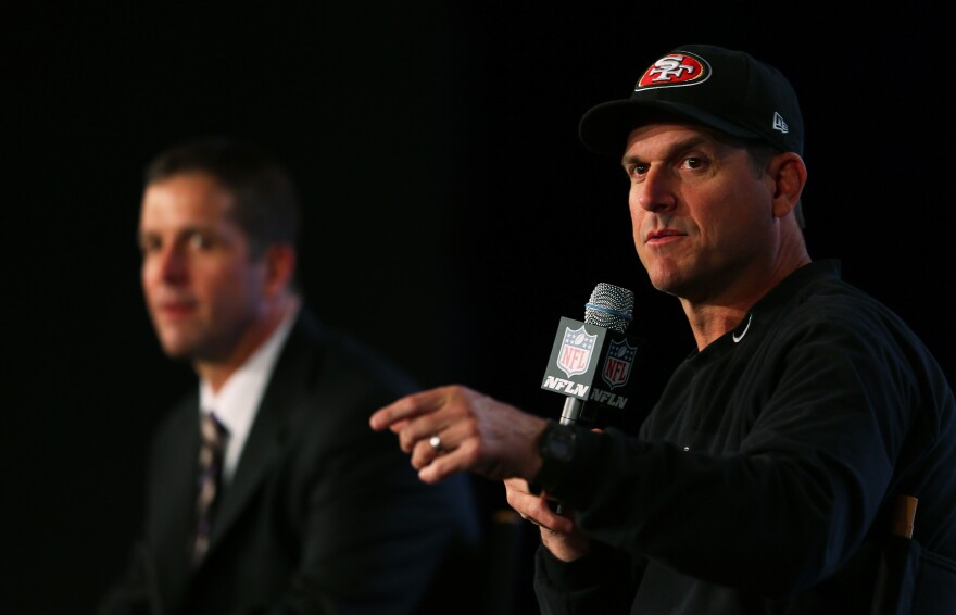 Head coach John Harbaugh (Suit-Wearing Brother) of the Baltimore Ravens and Head coach Jim Harbaugh (Hat-Wearing Brother) of the San Francisco 49ers speak to the media on Feb. 1.