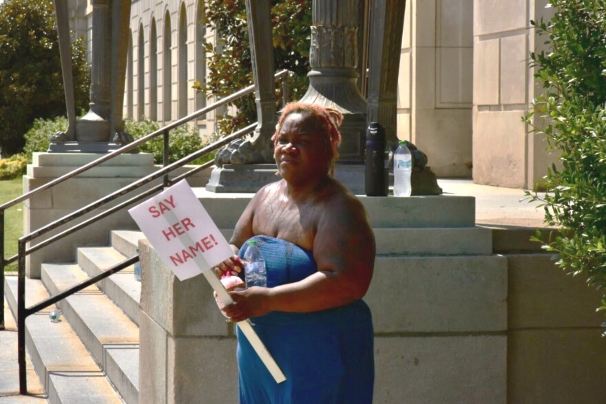 A Black woman stands with a sign that reads "Say Her Name!" She is outside a sentencing hearing for Brett Hankison, who was part of the deadly middle of the night raid at Breonna Taylor's apartment in March 2020.