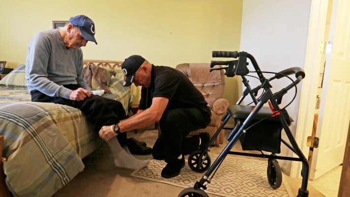 FILE - Caregiver Warren Manchess helping Paul Gregoline with his shoes and socks, in Noblesville, Ind., Nov. 27, 2013. (AP Photo/Darron Cummings, File)