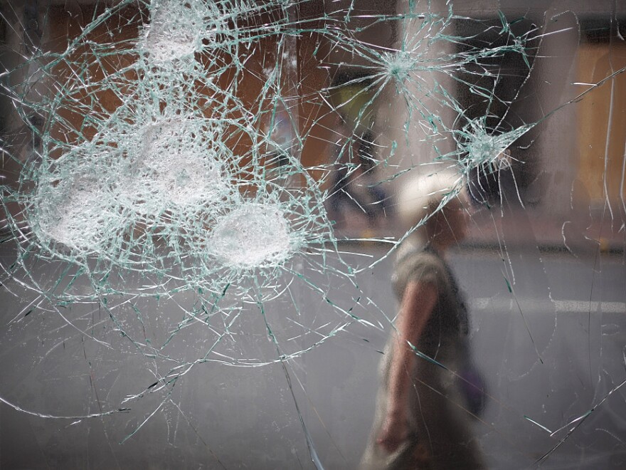 A woman walks past a broken cafe window in London earlier today (Aug. 10, 2011).