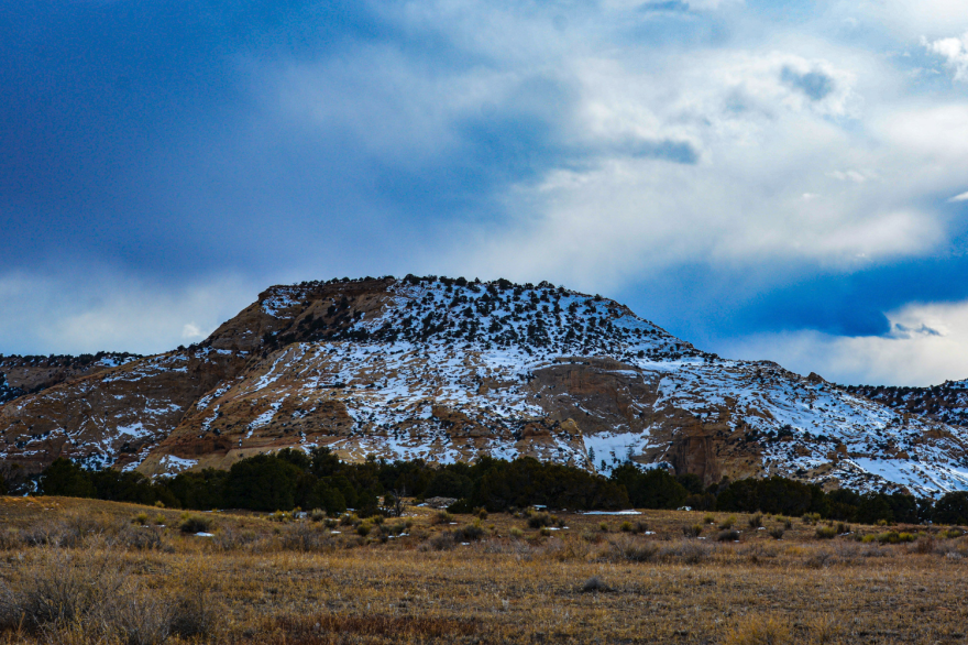 A small, rocky peak with some snow on it in an arid landscape.