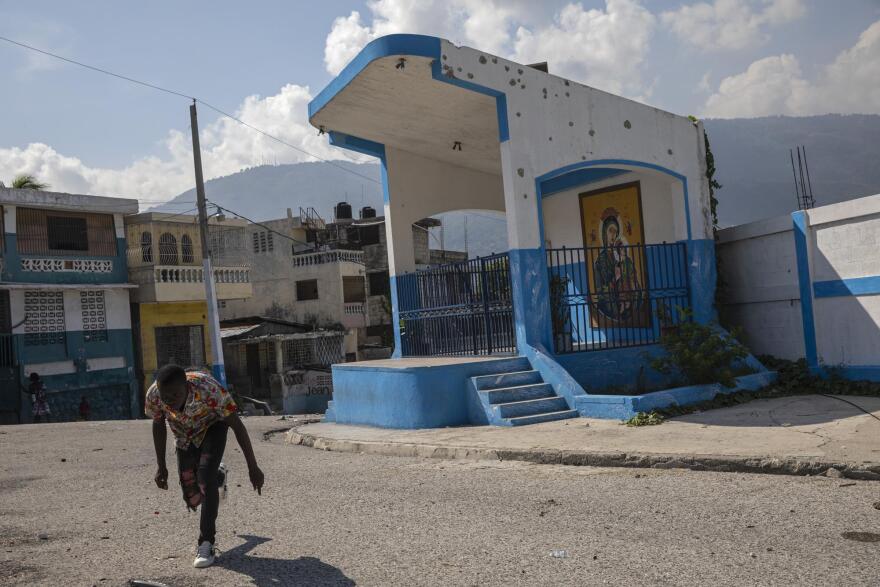  Near a bullet-pocked Catholic shrine, a Haitian man keeps low to avoid gunshots as he runs across a gang-controlled street in Port-au-Prince this month.