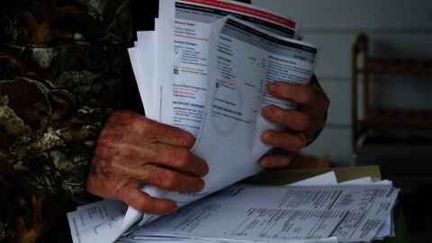 Eddie Lejuine holds a stack of utility bills on the front porch of his home in Hackberry, Louisiana, on Friday, January 23, 2026. Lejuine said that an increase in his electricity bills, combined with a decrease in his fishing catch, may force him to move.