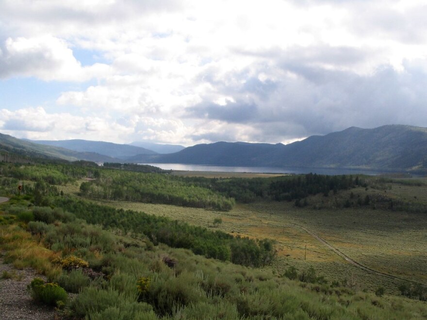 View overlooking a high, green mountain valley with a placid lake in the distance.