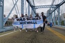 Marchers carry a sign reading "build bridges, not walls" as they walk across a suspension bridge
