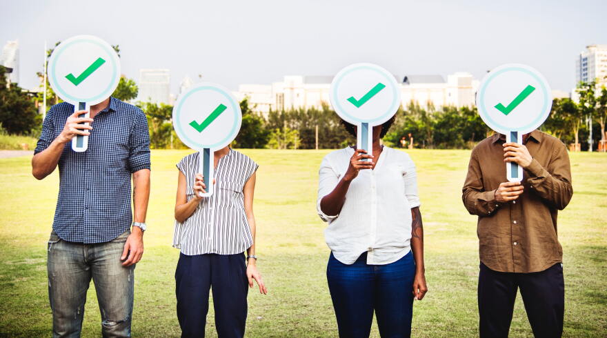 People of different genders and racial backgrounds hold check mark signs in front of their faces