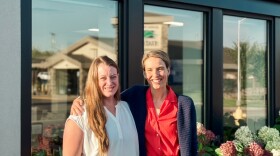 Two women stand outside in the sun in front of an urgent care clinic.
