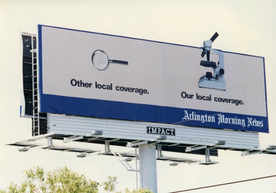  A white Arlington Morning News billboard holds two pictures: One of a magnifying glass that says, "Other local coverage," and another with a microscope that says, "Our local coverage."