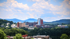 A distant view of Mission Hospital in Asheville with trees in the foreground and mountains in the background