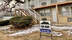 The photo shows a two-story rental unit with wooden stairs leading up to the second story in Des Moines, Iowa. Some snow is on the ground. A large sign out front says, "For rent" and has a name and phone number.