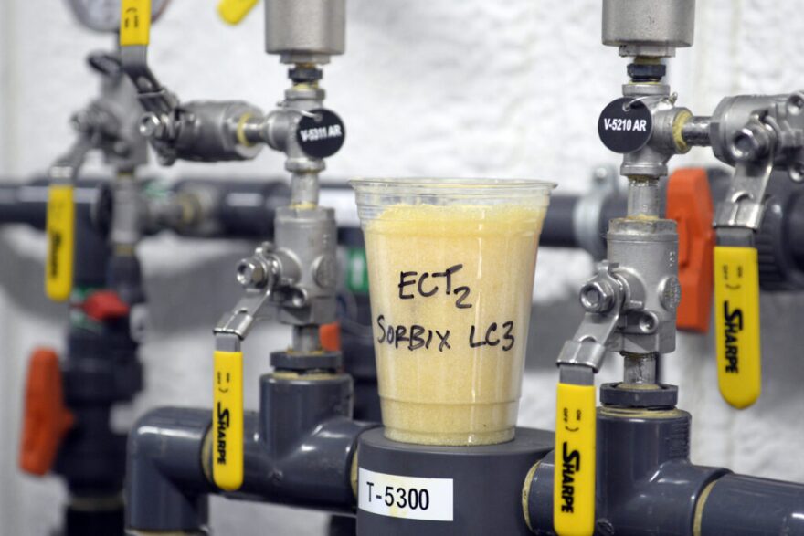 A cup full of gel-based material used to remove PFAS from water sits atop valves that control a groundwater remediation system. PFAS are a group of chemicals, some of which were formerly used in aircraft fire fighting foam. (U.S. Air Force photo by Ty Greenlees)