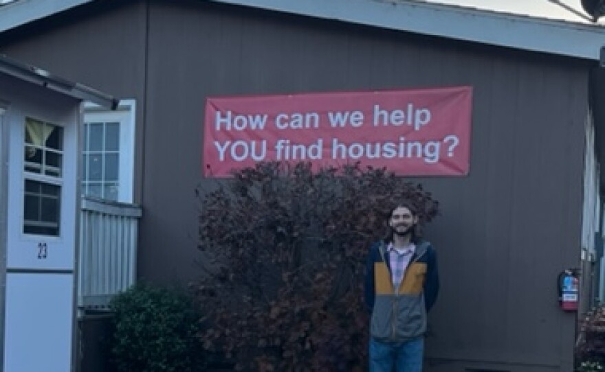 Ryan Murray in front of a "How can we help you find housing?" sign.