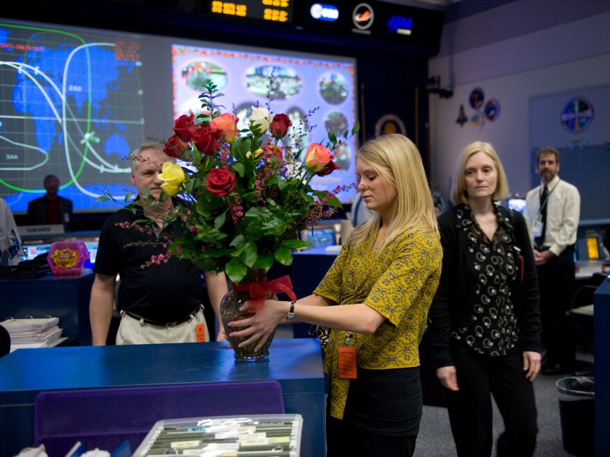 MacKenzie Shelton (center) sets up a bouquet of flowers commemorating the 100th mission they'd sent flowers to the Mission Control Center in 2009. Her parents, Mark (left) and Terry (right), look on.