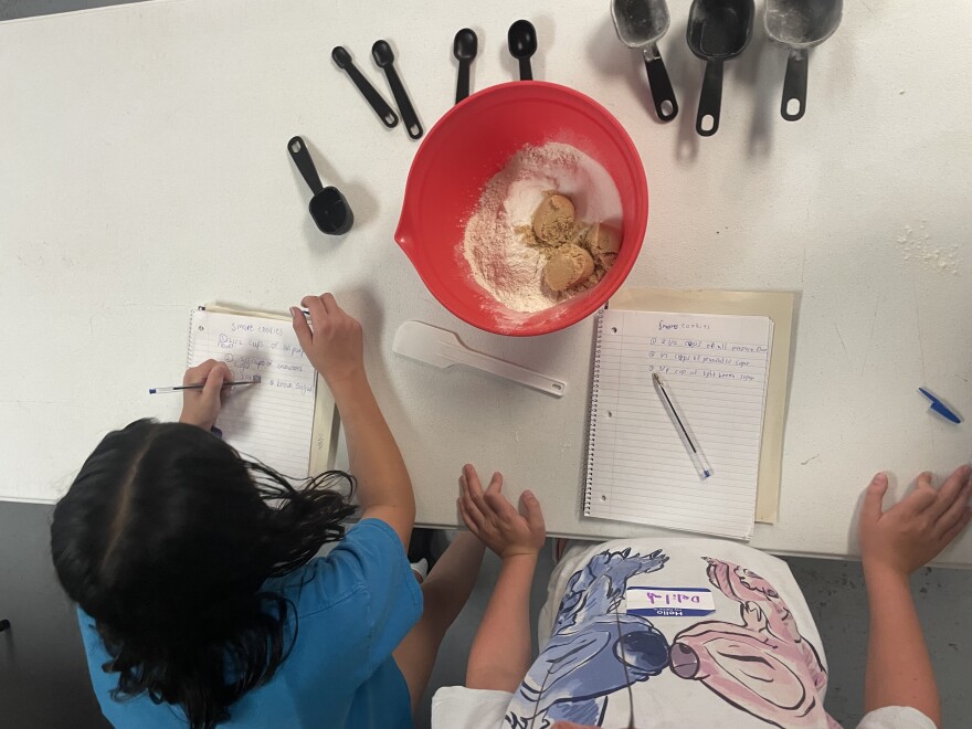 Paige Hickok and Delilah Kohrs preparing their cookie dough mixture and writing down the recipe in their notebooks