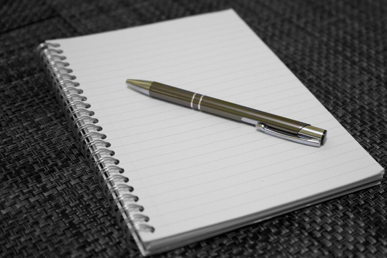 A pen lays on top of a spiral notebook.
