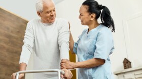 One more step. Cheerful positive friendly nurse standing near the elderly man and helping him to move around while being at work