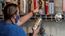On Friday, May 15, an employee following guidelines to wear a mask prepares a growler for a customer as businesses begin to reopen in Cincinnati in the wake of the coronavirus pandemic. 