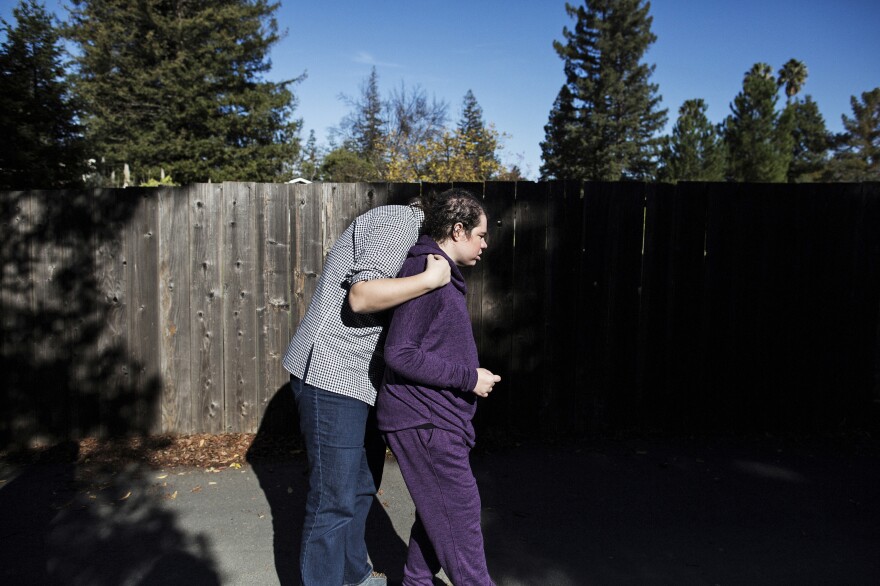 Natalie (right), who has a significant intellectual disability, is hugged by her part-time caretaker Mariah Hofstadter while being taken on a walk in the neighborhood.