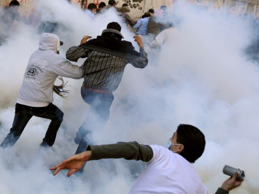 An Egyptian protester prepares to hurl a tear gas canister back at security forces as others run for cover earlier today in Cairo's Tahrir Square.