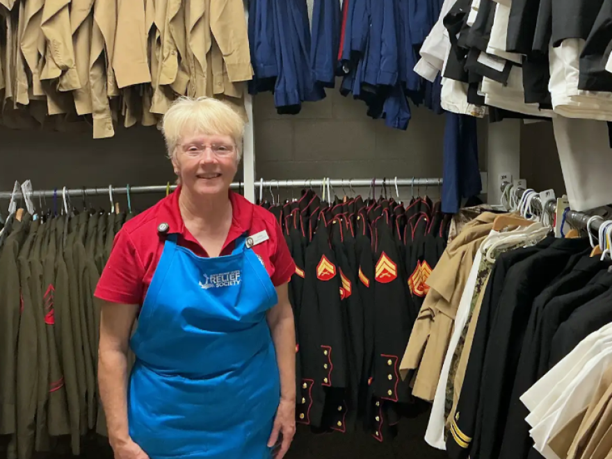Navy-Marine Corps Relief Society volunteer Audrey Faragher stands among racks of military uniforms at the organization’s thrift shop on NAS Pensacola. Faragher, who has volunteered at the shop since 2024, helps sort, price and organize donated items for military families.