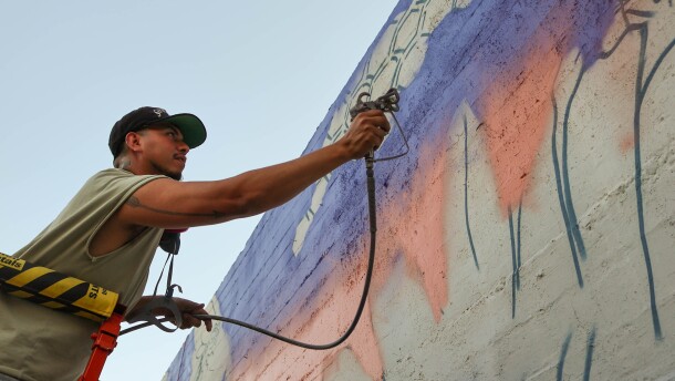 Joel Aguilar sprays orange paint onto his mural outside of Bella Luna, an Italian restaurant on Main Street.