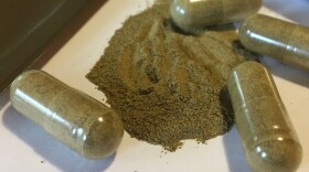 kratom capsules with some of the greenish substance on a white tray