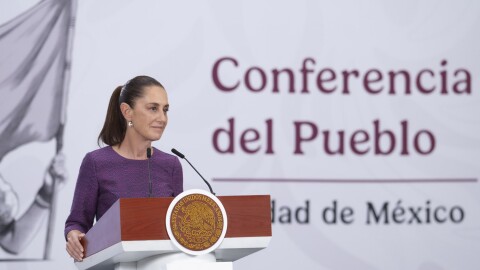 Woman with dark hair in purple dress stands behind brown and white podium