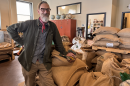 A man stands next to dozens of large burlap bags full of coffee beans. 