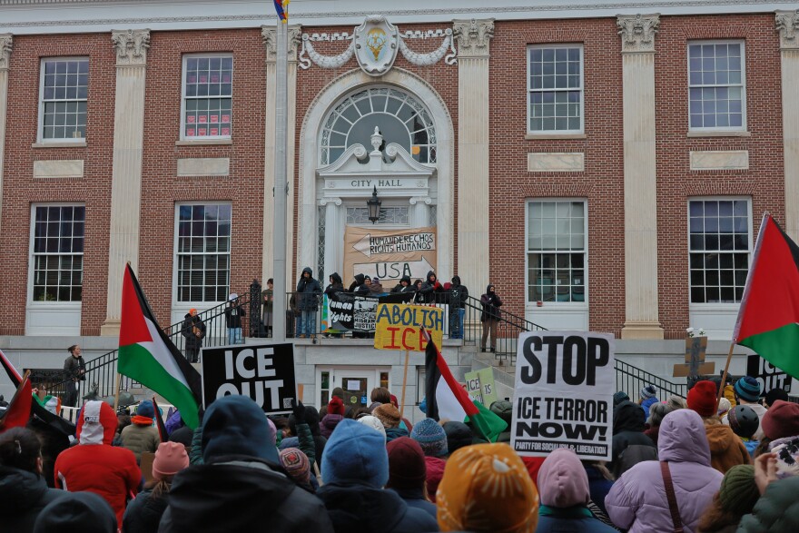 A crowd of protesters stand in front of Burlington City Hall. Some wave Palestinian flags and hold signed that read things like "ICE Out" and "Stop ICE Terror Now!"