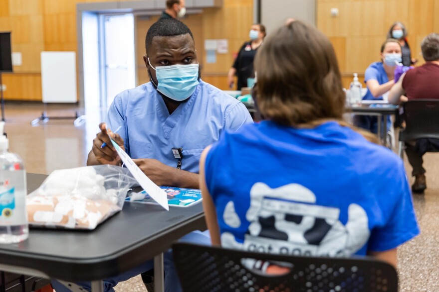 A man in blue scrubs speaks to someone about getting vaccinated.