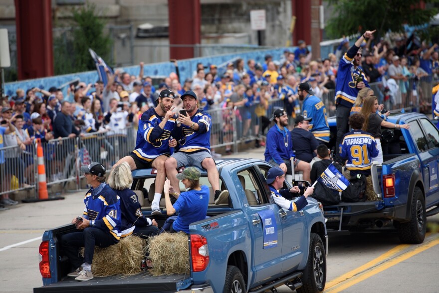 Fans cheer as Blues players, including defenseman Robert Bortuzzo, pictured left, are carried by pickup trucks through the throng.