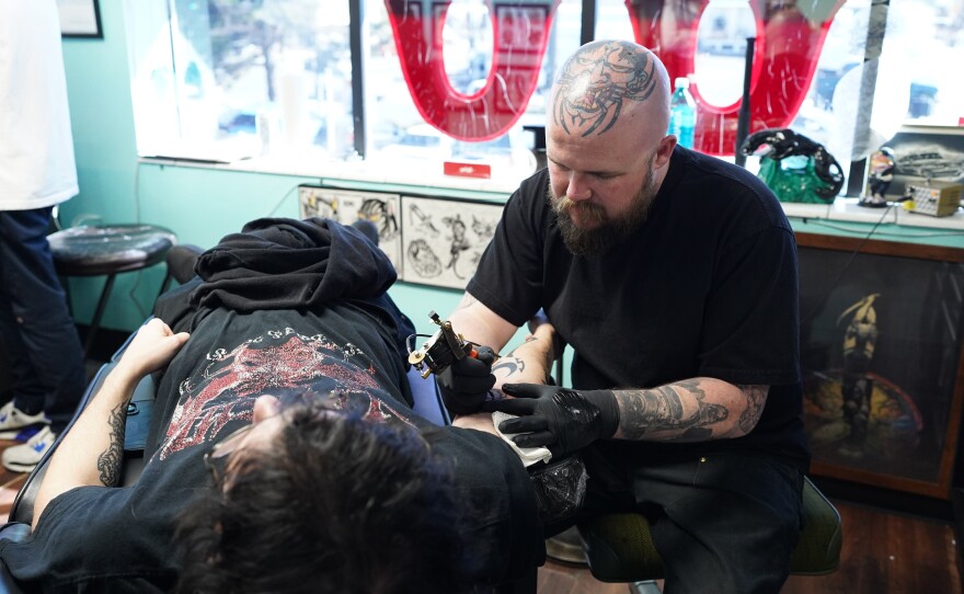 A bald tattoo artist with a colorful tattoo on his head tattoos a clients arm during a Friday the 13th tattoo event in Reno, Nevada.