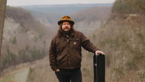 Tyler Westcott standing outside with his guitar case