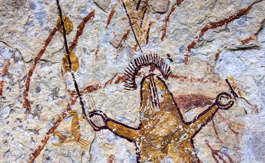 At Halo Shelter, this strikingly painted human-like figure appears to have a rayed halo hovering over its head. It wields a staff in its right hand with fingers resembling pincers.