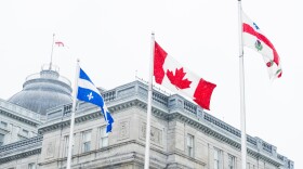 This is a horizontal, color, royalty free stock photograph of French Canadian flags waving in front of Old Montreal architecture in winter weather. Photographed with a Nikon D800 DSLR camera.