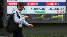 A man walks past monitors showing Japan's Nikkei 225 index, center, and a foreign exchange rate of the Japanese yen against the U.S. dollar at a securities firm in Tokyo, Tuesday, June 23, 2026.