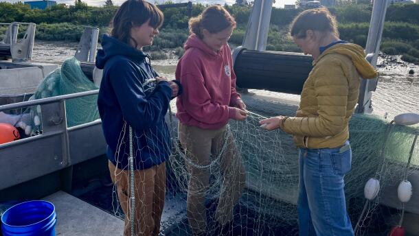 F/V Williwaw crew Kaija Dybdahl, Carolynn Pype, and Willow Oswald mend nets in the Dillingham Harbor.