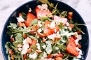 An arugula salad with strawberries, almonds and cheese.