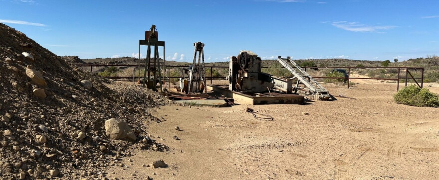 Abandoned, rusty well equipment in a shrubby desert area.